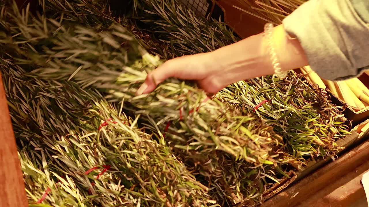 A hand picks fresh rosemary from a well-stocked supermarket display under warm lighting