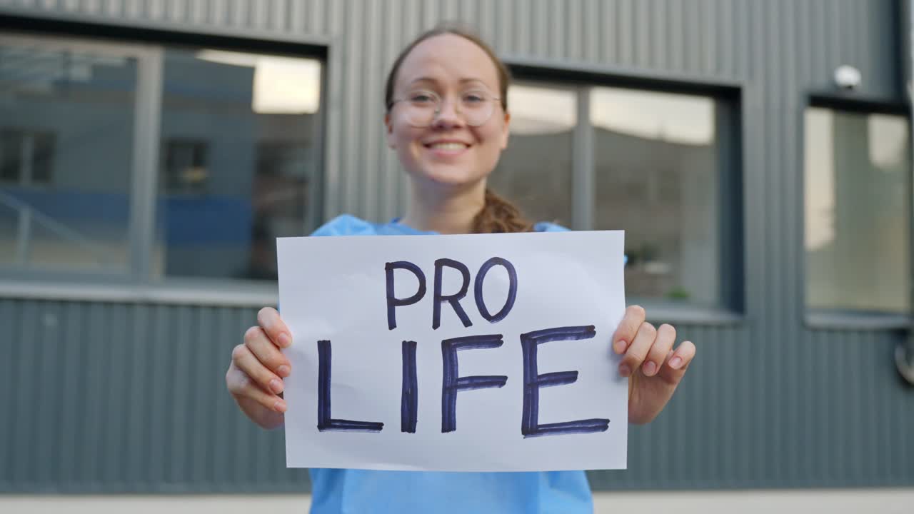 Professional Female Worker with a Clear Statement Holding Paper Reading "Pro Life" in Front of a Building Outside with Close Up Shot