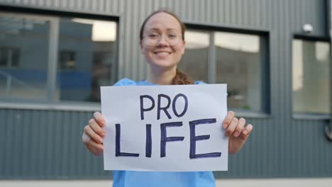 Professional Female Worker with a Clear Statement Holding Paper Reading &amp;quot;Pro Life&amp;quot; in Front of a Building Outside with Close Up Shot