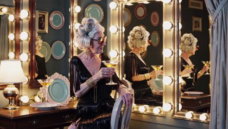 glamorous senior woman with stylish hairstyle and sunglasses enjoying a cocktail in a vintage dressing room, reflected in a mirror with lights