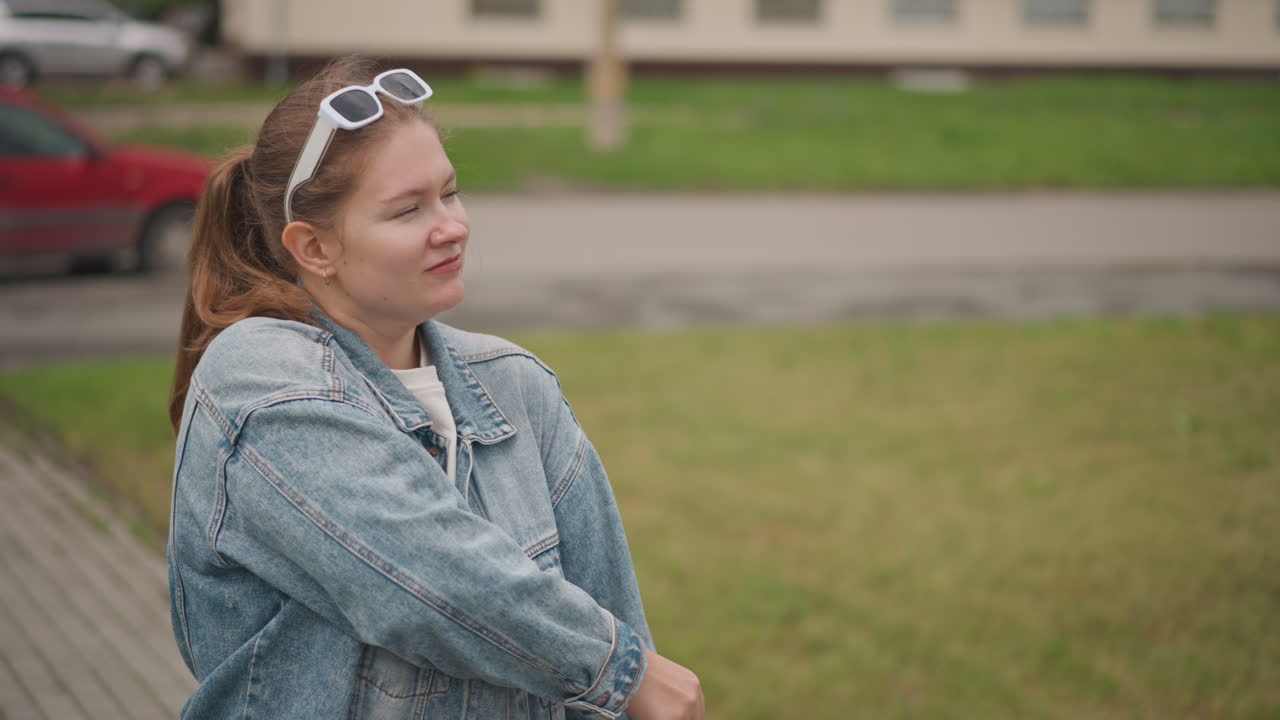Ung kvinde smiler og justerer sin mulepose på et byfortov, denimjakke og solbriller, selvsikker holdning, venligt udtryk, streetstyle-æstetik, afslappet stemning for indholdsskabelse, daglig pendling.