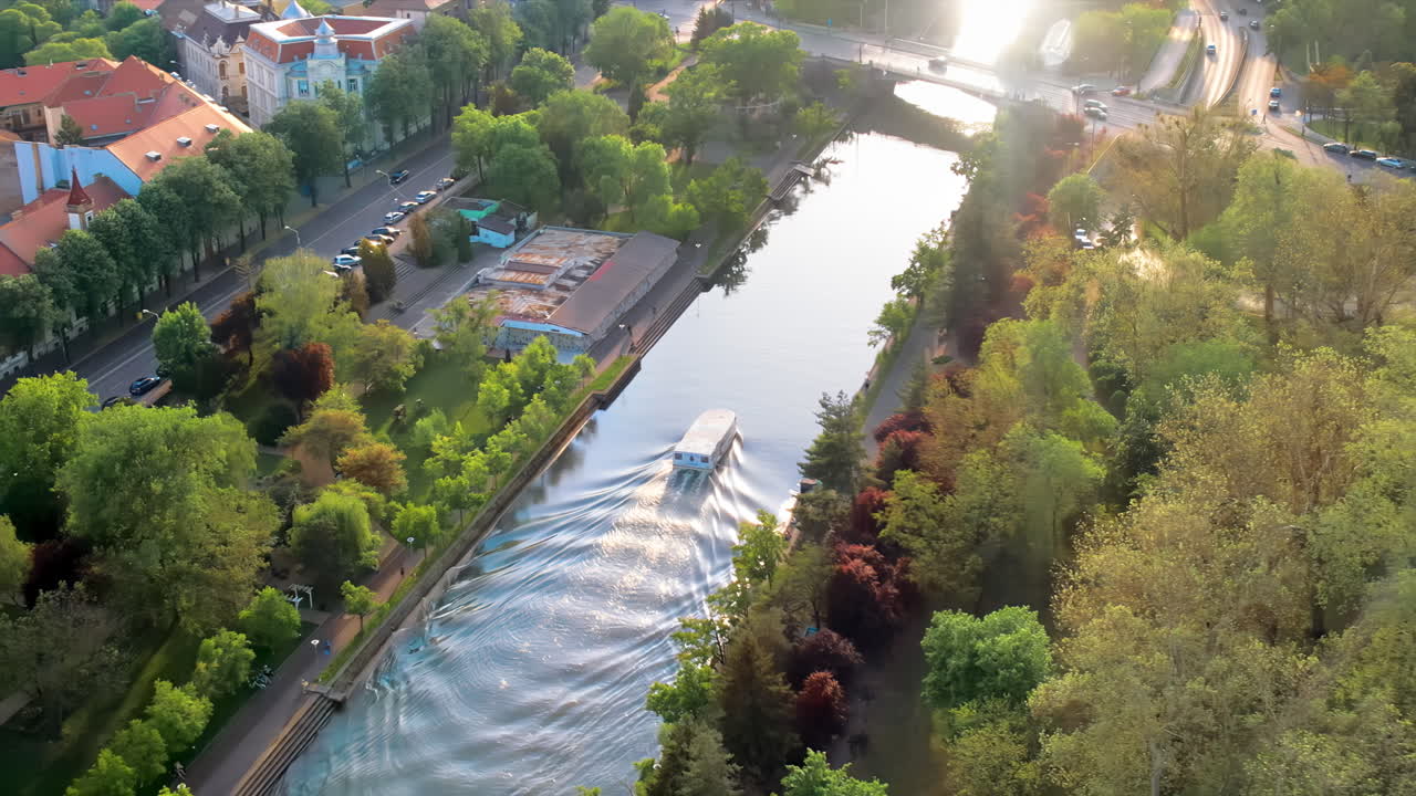 Aerial drone view of Bega river in Timisoara at sunset, Romania. View of the river with floating boat, greenery and buildings on the both sides of the river