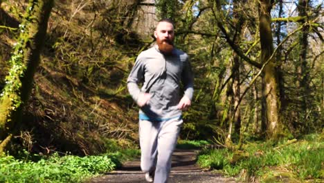 slow motion of bearded young man running up a forest then passing the camera