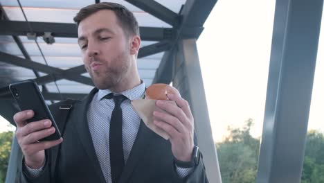 businessman eating a burger while using his phone
