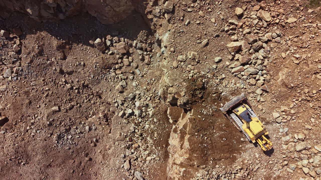 Macchinari pesanti lavorano in un cantiere in una cava di roccia, spostando terra e rocce durante le ore diurne in un'area remota.