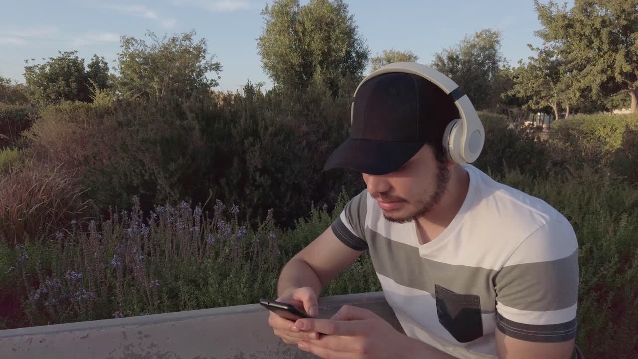 Smiling young man, listening music, checks his mobile, in a park