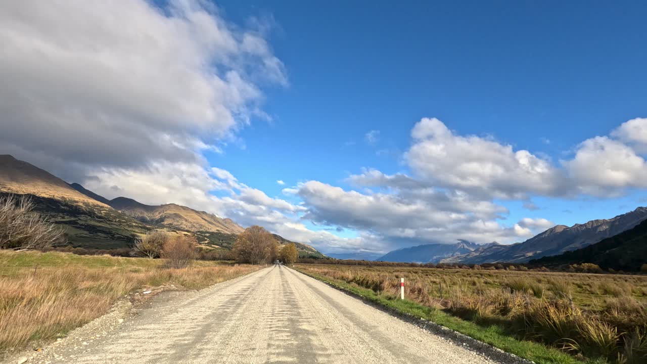 Visuale in avanti di un'auto su una strada sterrata di campagna, montagne, cielo blu, luce naturale, prospettiva stabile