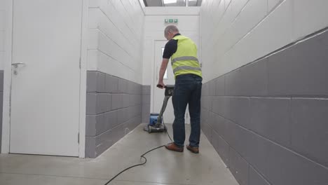 Man-in-yellow-high-visibility-vest-uses-machine-to-clean-building-floor