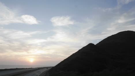 Zeitraffer-Von-Wolken,-Die-Sich-Bei-Sonnenuntergang-über-Einen-Hang-Und-Eine-Autobahn-Bewegen