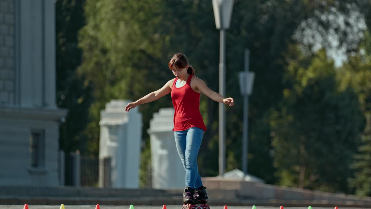 Giovane donna gira intorno ai coni sui pattini a rotelle, elemento slalom, incrocio. Bella donna si allena all'aperto, pattini a rotelle. 4k, 10bit, ProRes