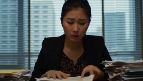 a woman in formal attire appears stressed as she sorts through an enormous pile of documents in a high-rise office filled with natural light. the atmosphere suggests a hectic work day.