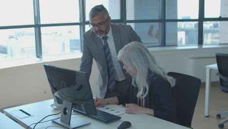 Focused-male-boss-and-female-manager-discussing-reports