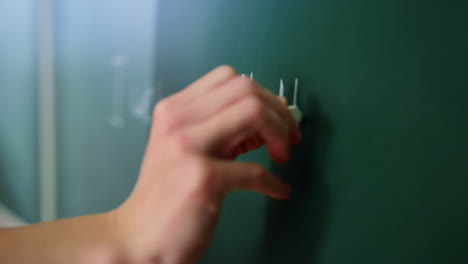 closeup teacher arm writing on blackboard in class. woman drawing on chalkboard