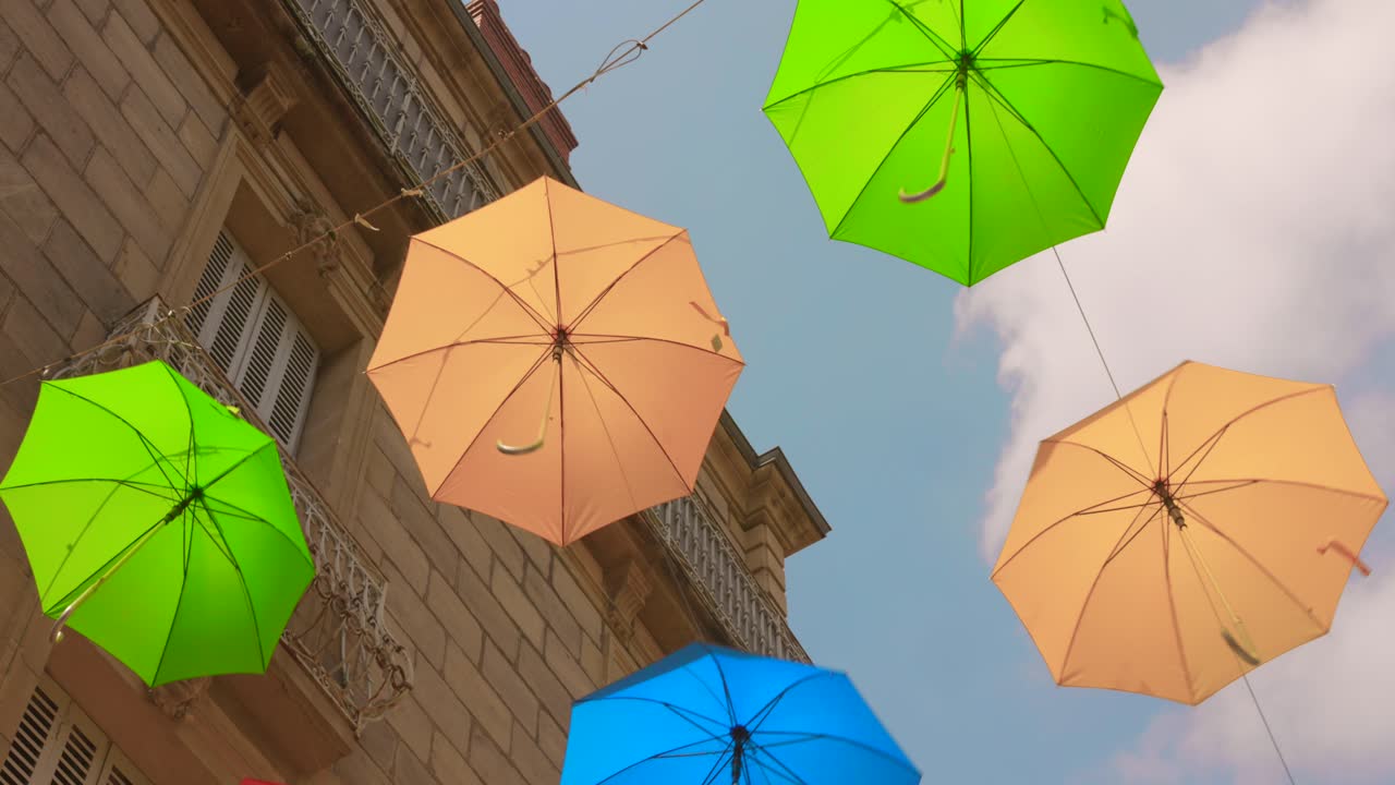 Vibrant summer umbrellas hanging above a historic street in Brive-la-Gaillarde, casting playful shadows on the stone buildings