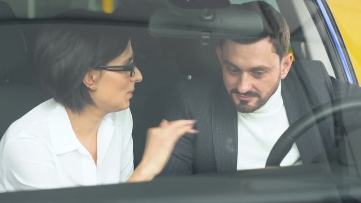 Stylish businessman sitting in car salon and talking with female car dealer. Young confident guy choosing automobile in showroom