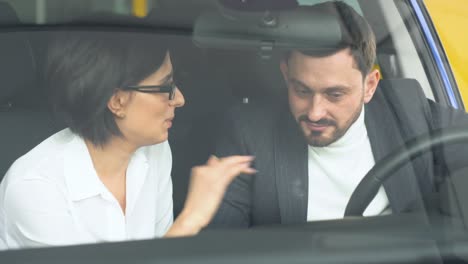 stylish businessman sitting in car salon and talking with female car dealer. young confident guy choosing automobile in showroom