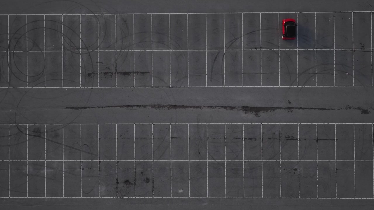 Drone shot of red car on a empty parking lot.