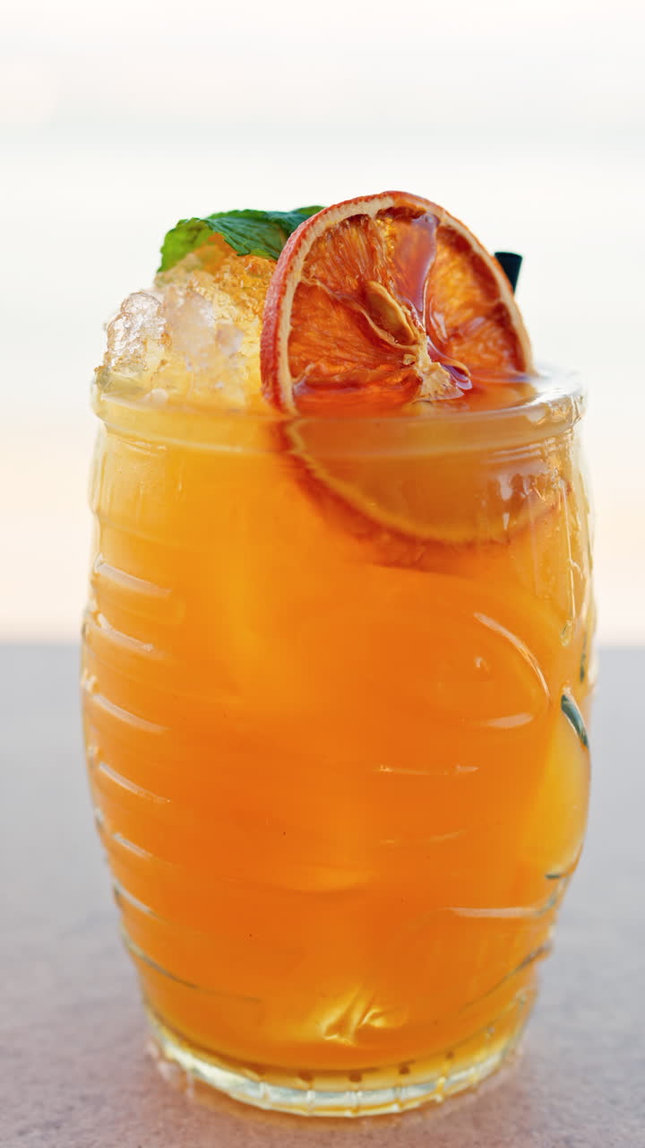 Primo piano di un cocktail arancione su un tavolo con una vista sfocata del mare sullo sfondo. Verticale