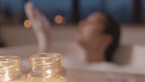 욕조에서 목욕을 하는 흐릿한 여성을 배경으로 촛불을 가까이서 볼 수 있습니다.