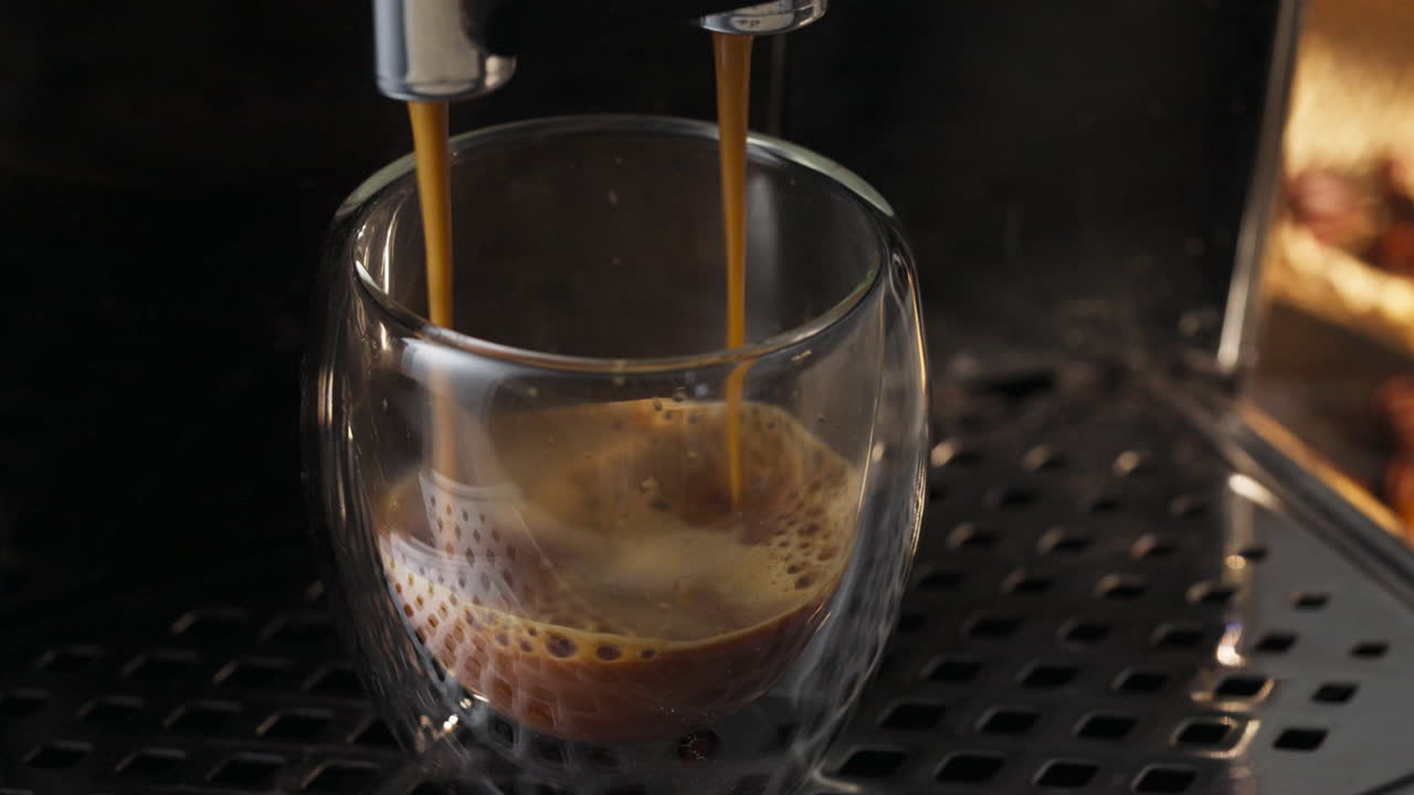 Person pouring a machine coffee in a glass tumbler. Close up