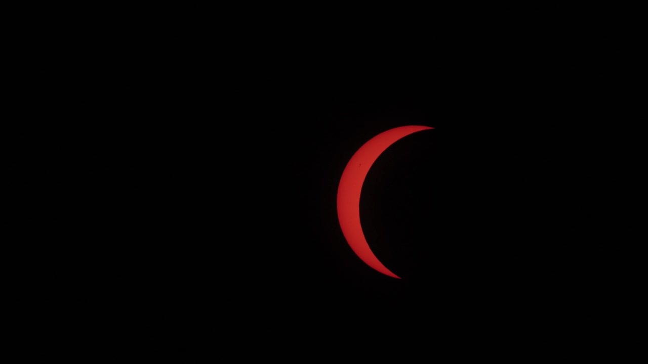 Dramatic close-up footage captures the vivid red crescent of the sun during the full eclipse phase, set against a deep black sky. Perfect for science, astronomy, or celestial event visuals.