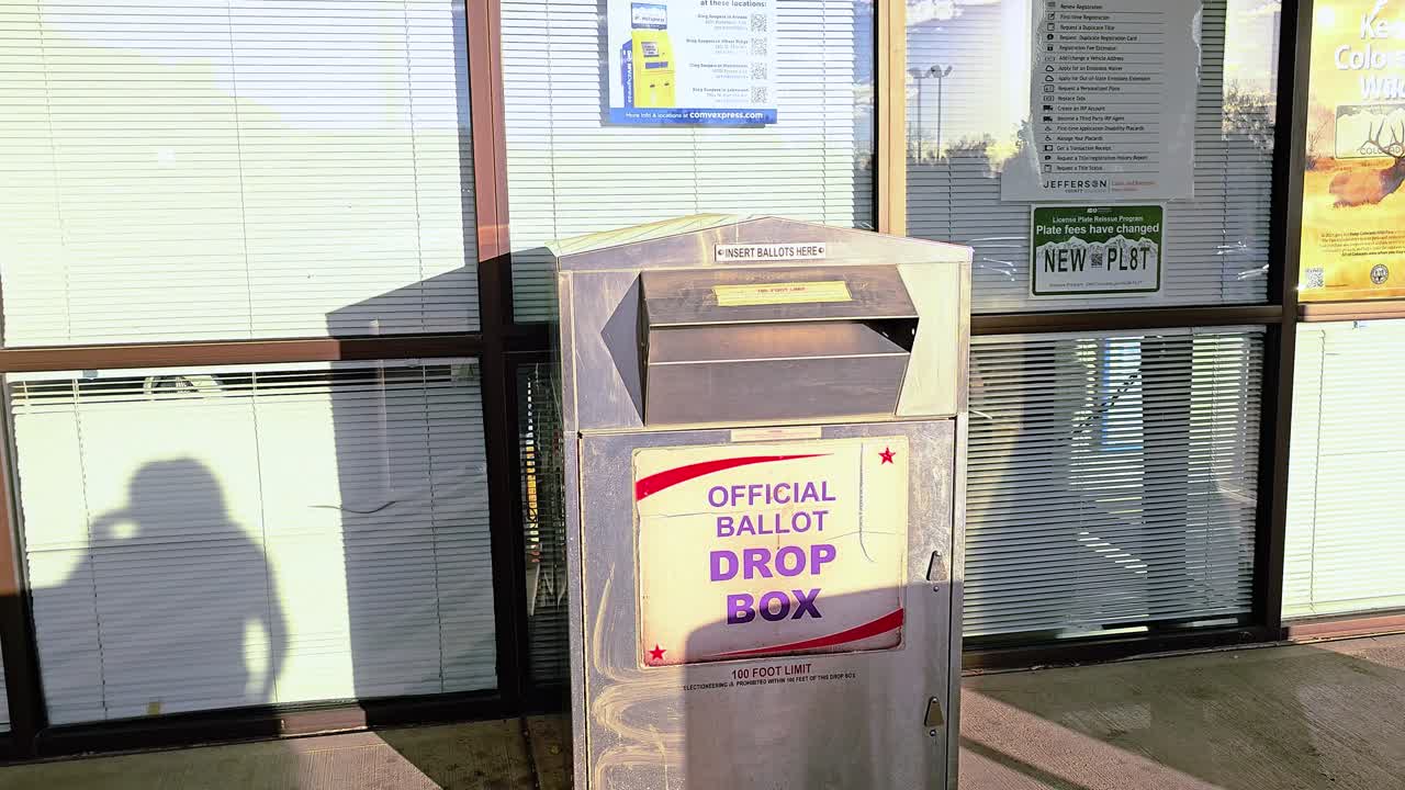 히스패닉 여성이 대통령 선거에서 민주 정부 캠페인을 위한 공식 투표소 드롭 박스 표지판과 함께 투표소의 슬롯에 우편 투표용지를 던져서 선거에 투표합니다.