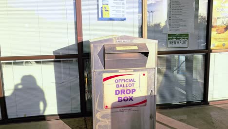 hispanic woman votes in election by casting mail-in ballot letter in slot at voting booth with offical ballot drop box sign for democratic government campaign in presidential race