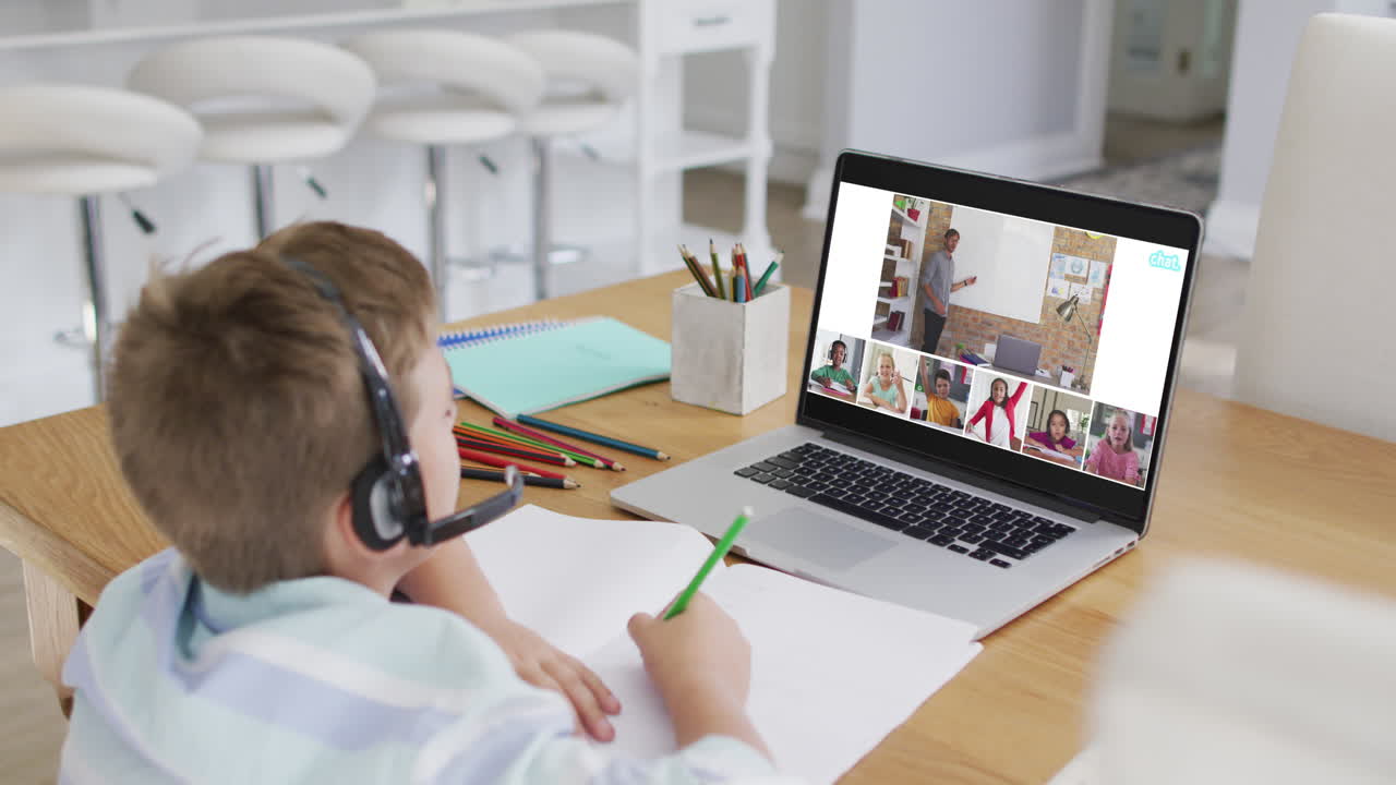 Schoolboy using laptop for online lesson at home, with diverse teacher and class on screen