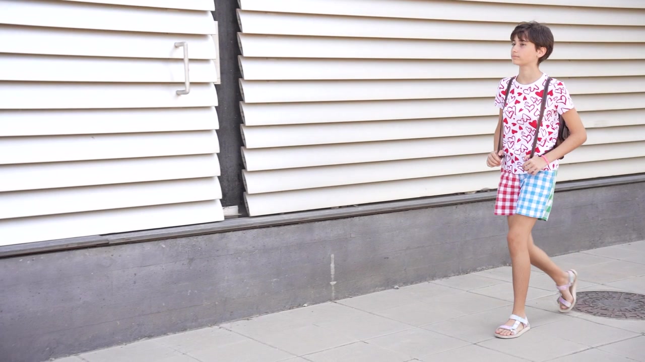 Un giovane ragazzo sicuro di sé cammina felicemente per una vivace strada cittadina durante una giornata colorata