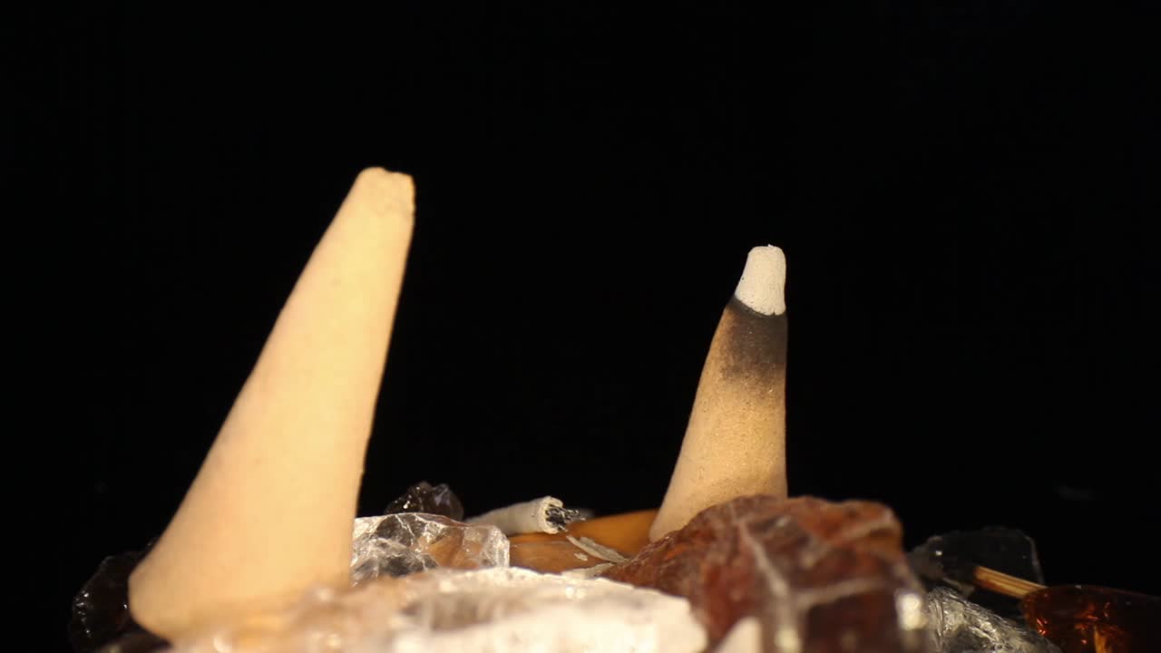 dos conos de incienso en un jardín de rocas decorativas, empujando hacia un cono iluminado donde el humo apenas es visible