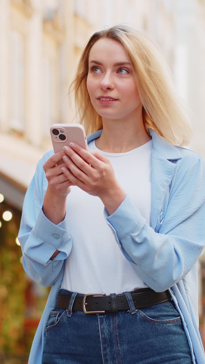 Donna felice che usa lo smartphone, scrive, manda messaggi, applicazioni di social media, e-mail in una strada della città.