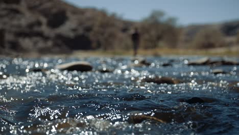 slow motion hand held shallow depth of field shot of a a river running in africa as a man walks in the background.