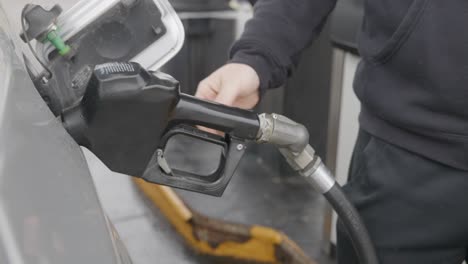 gasolinera hombre caucásico blanco con anillo de bodas llenando coche plateado con boquilla de gas insertada en el tanque y luego ajustando el mecanismo de bomba automática dos veces y luego retrocediendo