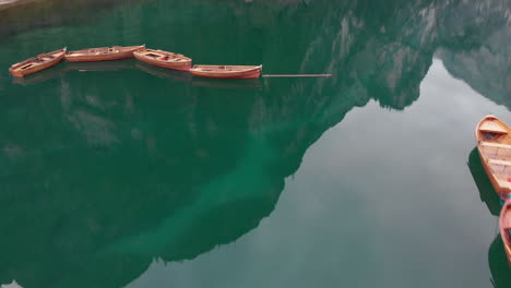 Toma-Aérea-De-Un-Dron-Sobre-Barcos-Alineados-En-El-Lago-Braies-En-Los-Dolomitas,-Italia