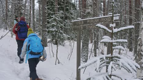 Pirunkirkko-and-simonlampi-signs-in-winter-forest-in-Finland,-people-walking