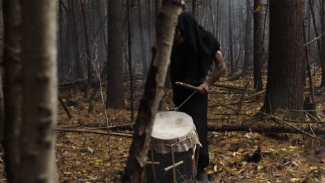 mysterious man playing music with a rustic homemade drum in the middle of the forest