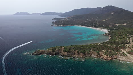 costa de cerdeña con aguas azules claras y montañas en el fondo, vista aérea