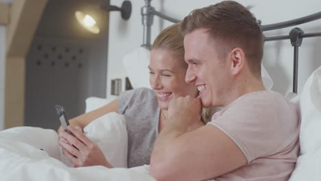 pareja en la cama con pijama mirando el teléfono móvil juntos