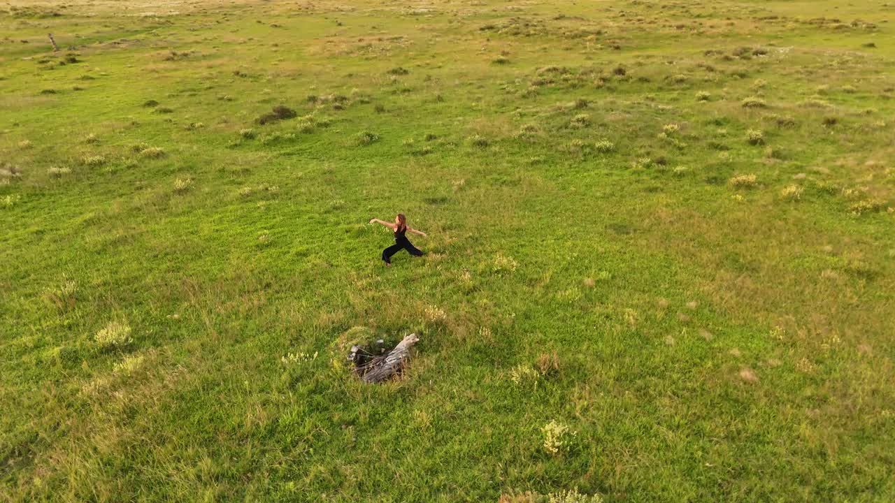 Woman doing stretch exercise and yoga on grass field during golden sunset in Uruguay. Aerial orbit shot.