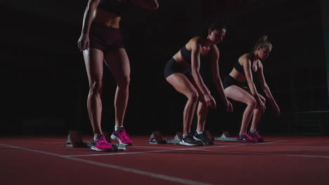 female runners at athletics track crouching at the starting blocks before a race. in slow motion.