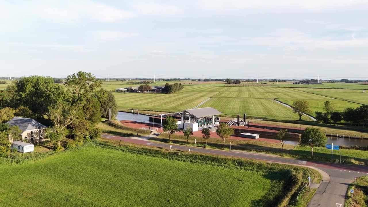 Serena vista aerea di un moderno sistema di chiuse di canale circondato da rigogliosi campi verdi e prati nel paesaggio rurale dei Paesi Bassi, con turbine eoliche in lontananza che generano energia rinnovabile