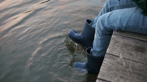 vista cercana de las botas de un niño en el agua de un lago