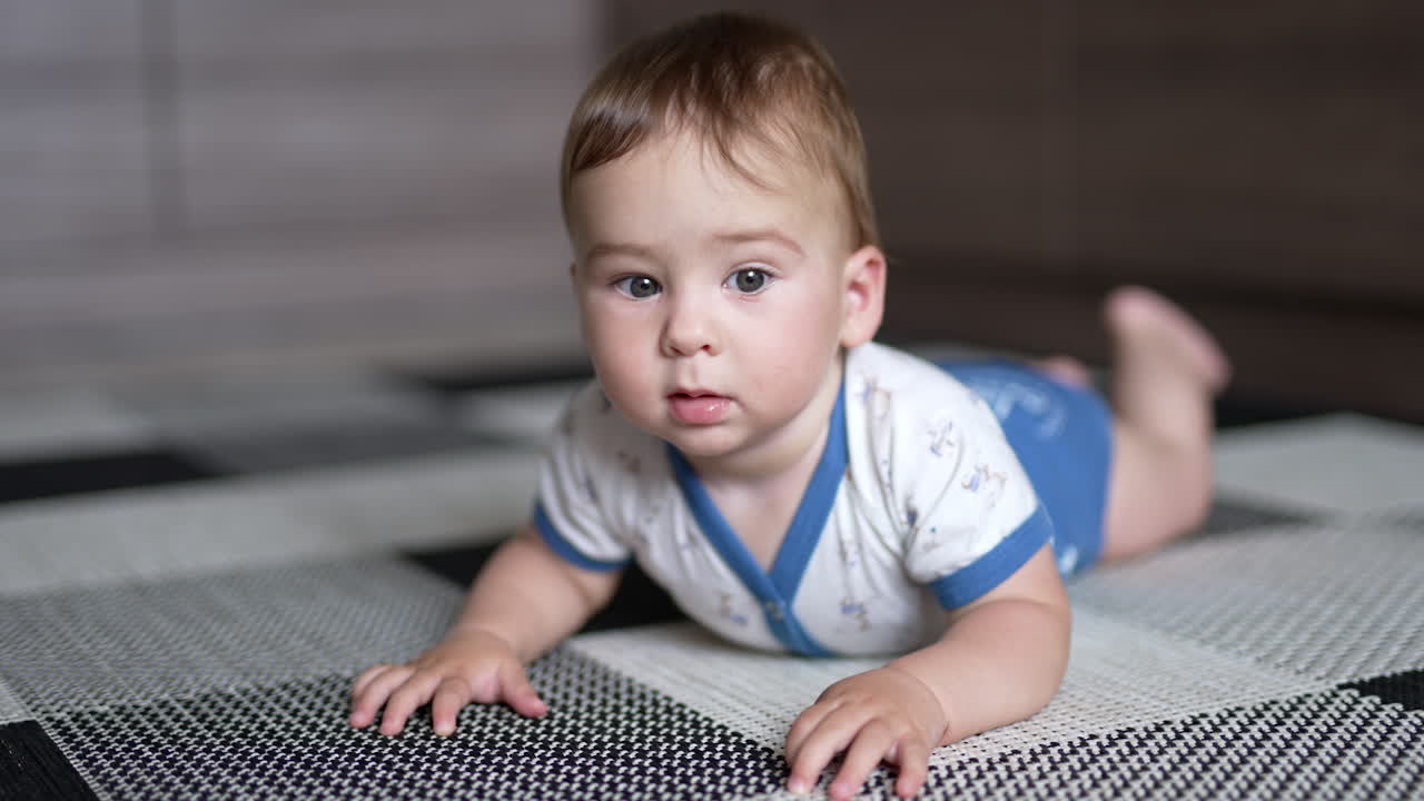Cute lovely kid lying on the floor trying to crawl. Adorable kid stops looking at camera with interest. Close up.