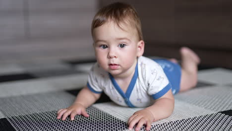 cute lovely kid lying on the floor trying to crawl. adorable kid stops looking at camera with interest. close up.