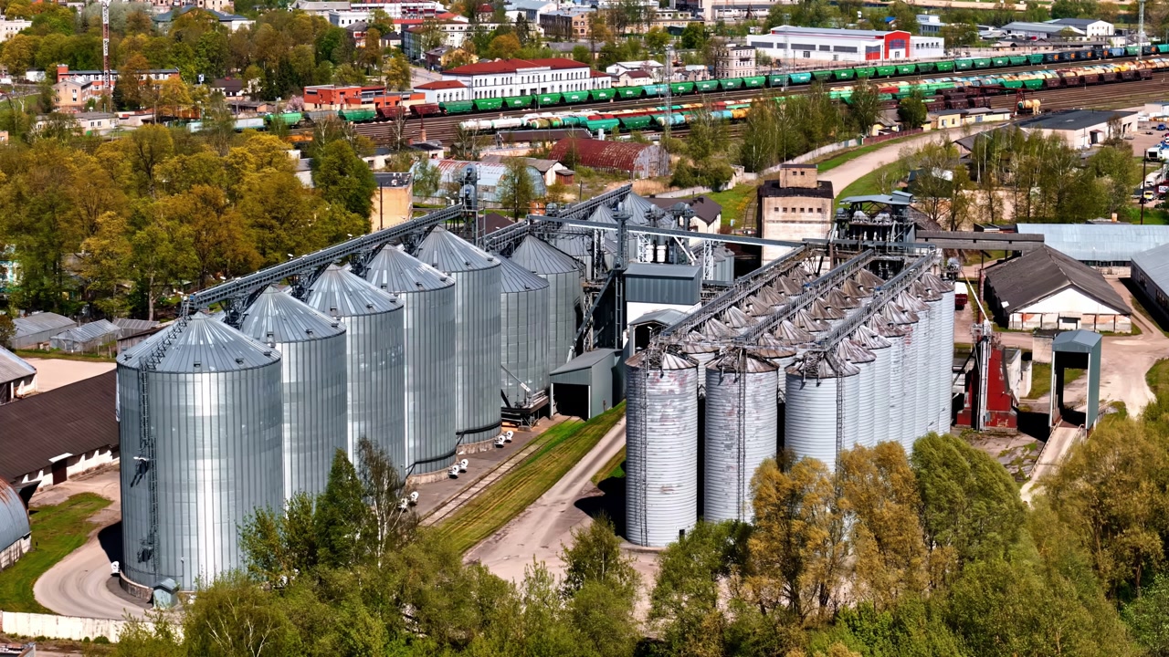 Aerial of large industrial grain elevator complex with metal silos and nearby rail yard