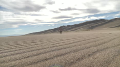 wide cinematic shot of sand blowing while blurred traveler approaches