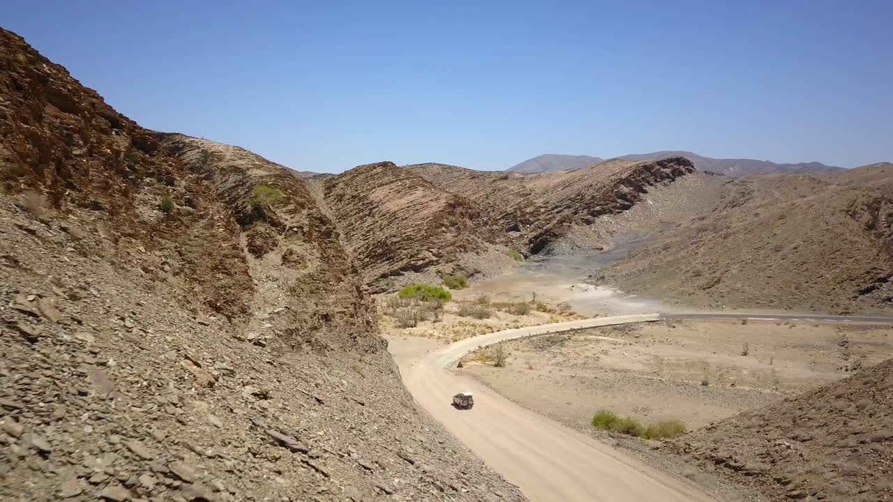 4K footage of a jeep driving along a dusty road in Namibia, captured from a drone following the vehicle. The breathtaking rocky landscape and expansive views the rugged beauty of this African terrain.