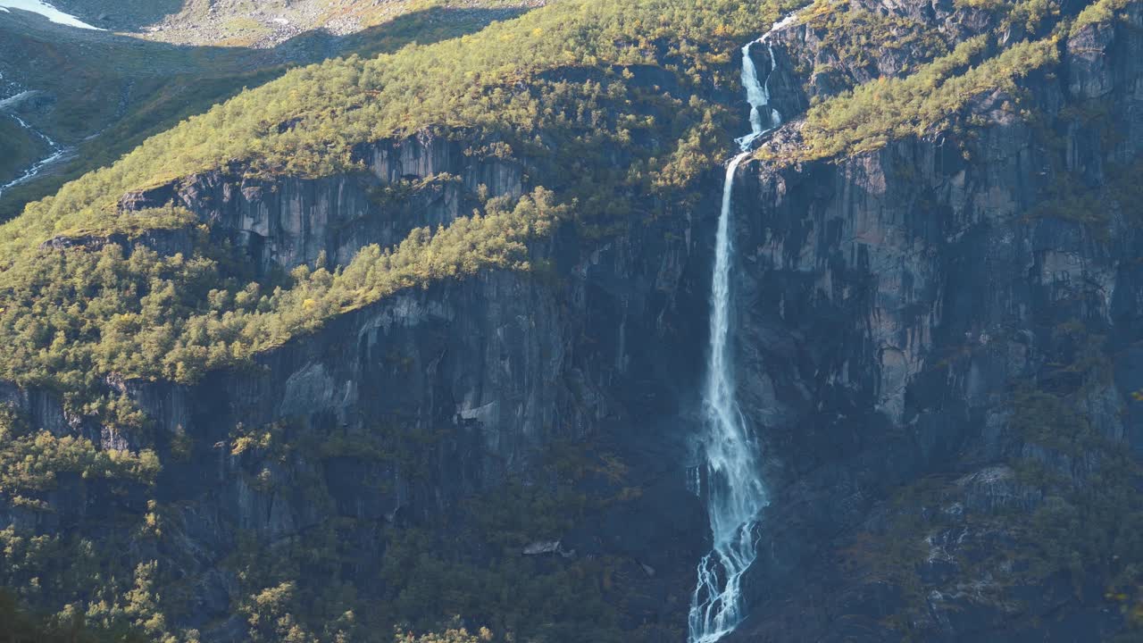 Splendida ripresa di una lunga cascata, che scende da grandi montagne, in una giornata di sole con telecamera in leggero movimento laterale