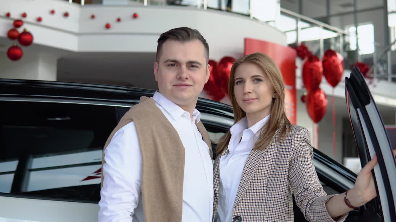 Happy couple at a car dealership with a new car in the background