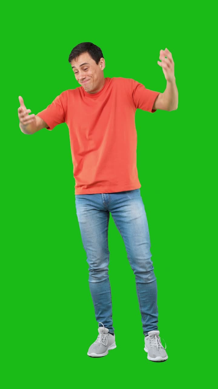 A man in an orange t-shirt and jeans posing against a green screen